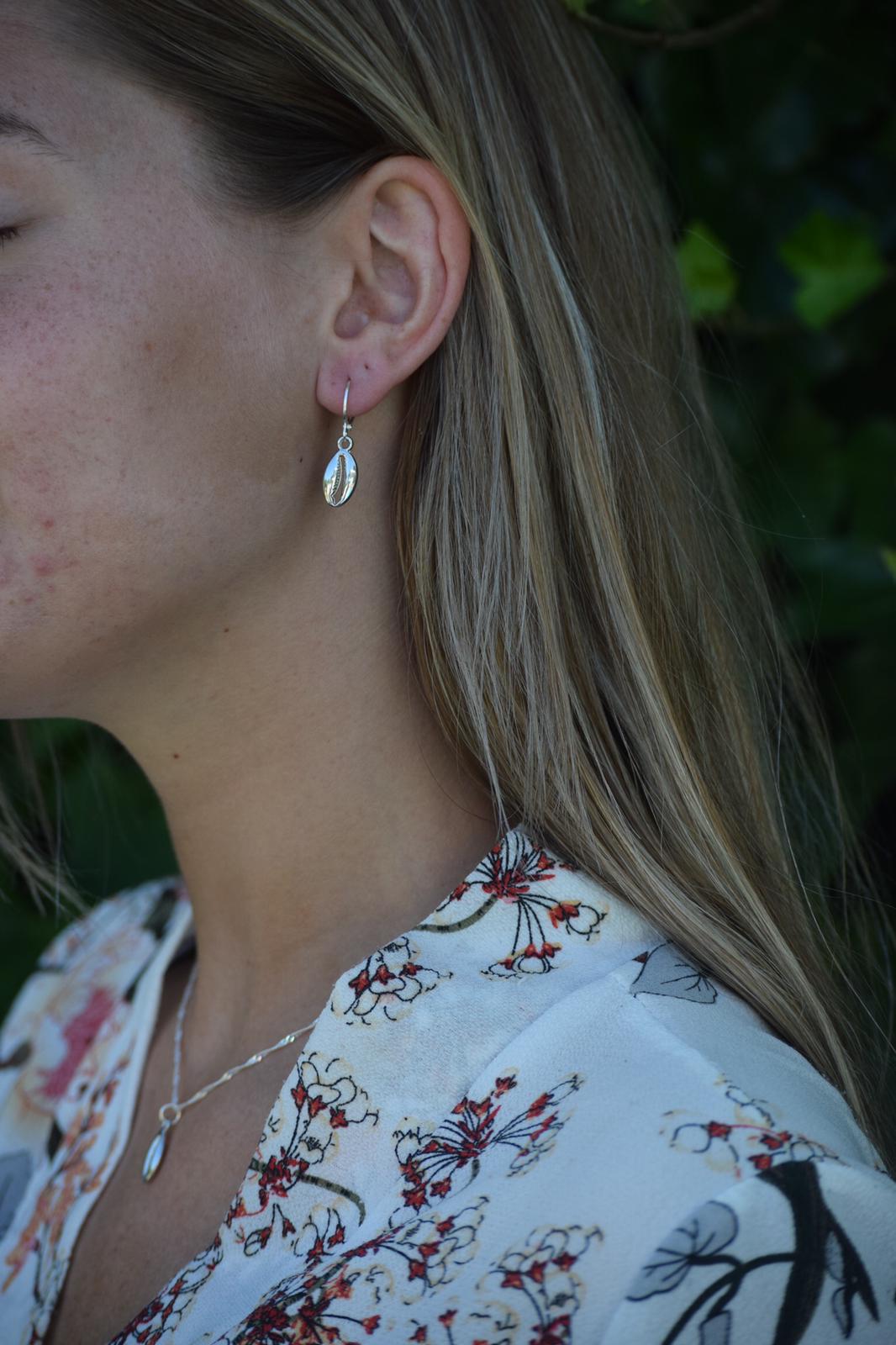 zomerse foto van model in de natuur met blond haar en een roestvrijstalen sieraden set in het zilver bestaande uit oorbellen met een schelp en een ketting met een schelp.