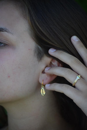 close up van model met goudkleurige schelp oorbellen en goudkleurige coin ring.